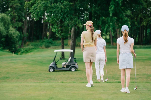 Vista trasera de las mujeres con equipo de golf caminando sobre césped verde en el campo de golf - foto de stock