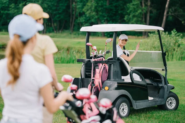 Selective focus of woman in golf cart greeting friends at golf course — Stock Photo