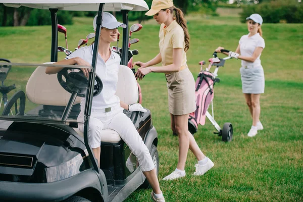 Enfoque selectivo de las jugadoras de golf en gorras en el carrito de golf en el campo de golf - foto de stock