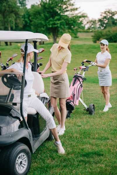 Jogadoras de golfe em bonés no carrinho de golfe no campo de golfe — Fotografia de Stock