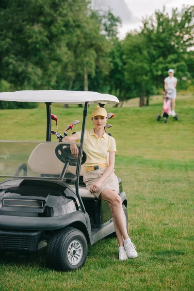 Foco seletivo do jogador de golfe feminino no carrinho de golfe no gramado verde — Fotografia de Stock