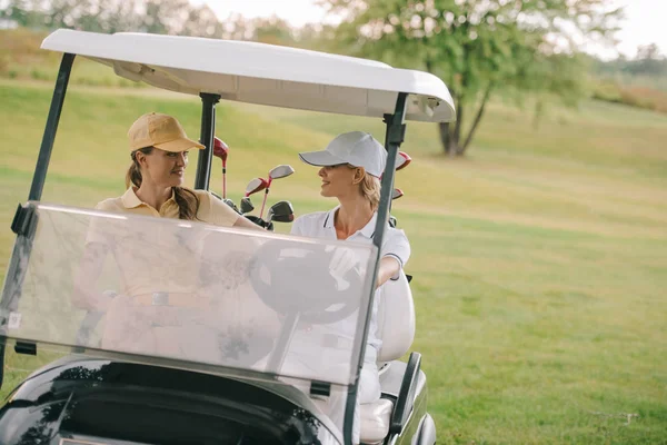 Улыбающиеся женщины-гольфистки на гольф-каре на поле для гольфа — стоковое фото