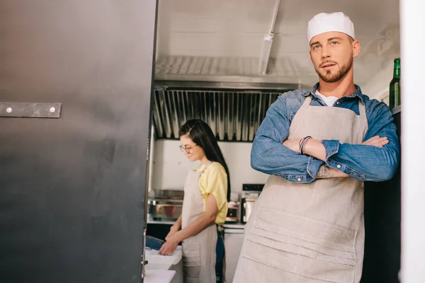 Chef masculino de pé com braços cruzados, enquanto colega do sexo feminino trabalhando atrás em caminhão de alimentos — Fotografia de Stock