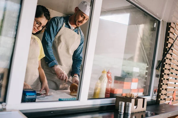 Sonrientes jóvenes trabajadores y trabajadoras trabajando juntos en camión de comida - foto de stock