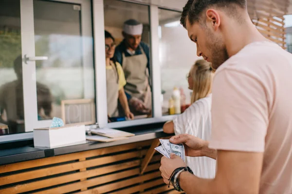Young man counting money while standing in line at food truck — Stock Photo