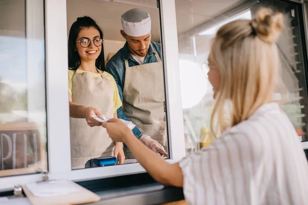 Junge Frau bezahlt lächelnde Arbeiterin in Food-Truck — Stockfoto