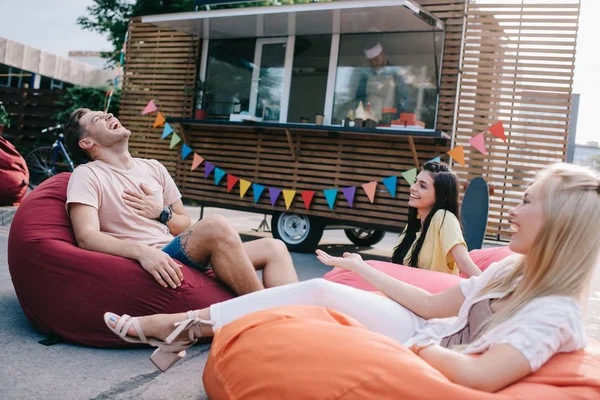 Happy young friends laughing while sitting on bean bag chairs near food truck — Stock Photo