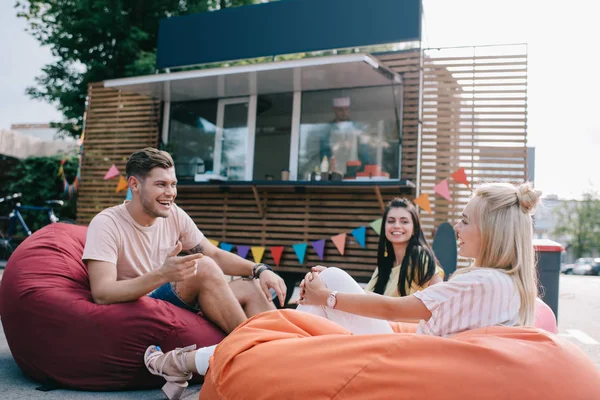 Happy young friends talking while sitting on bean bag chairs near food truck — Stock Photo