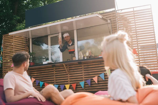 Chef felice che lavora nel food truck e sorride ai giovani clienti fuori — Foto stock