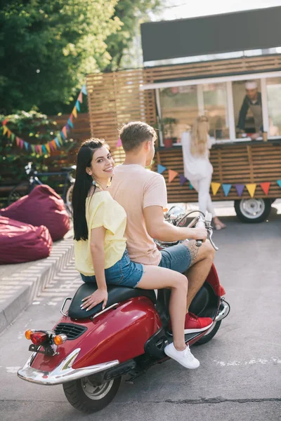 Happy couple sitting on scooter near food truck on street — Stock Photo