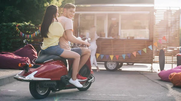 Happy couple sitting on motorbike near food truck on street — Stock Photo