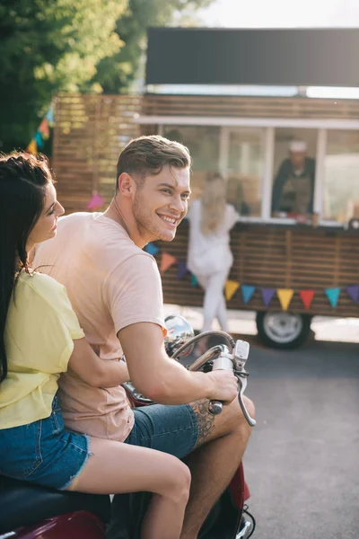 Улыбающаяся пара, сидящая на мотоцикле возле фургона с едой на улице — стоковое фото
