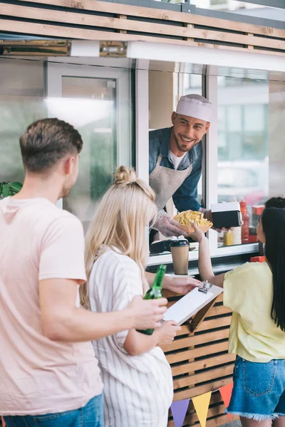 Chef sorridente dando patatine fritte alla ragazza dal camion cibo — Foto stock