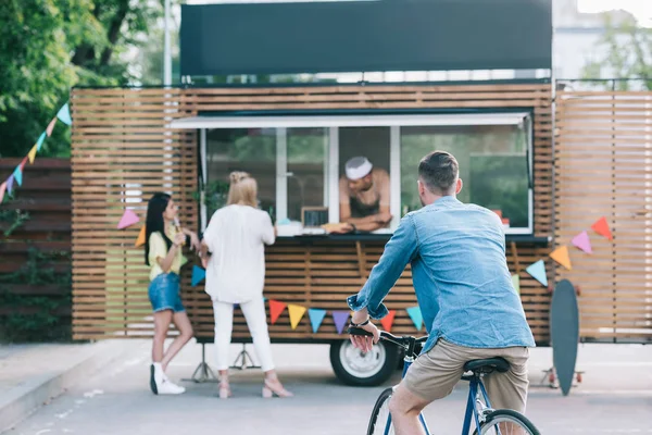 Rückansicht eines Mannes, der in der Nähe eines Foodtrucks auf einem Fahrrad sitzt — Stockfoto
