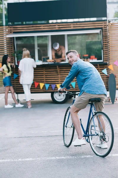 Schöner Mann sitzt auf Fahrrad in der Nähe von Food Truck und blickt in die Kamera — Stockfoto