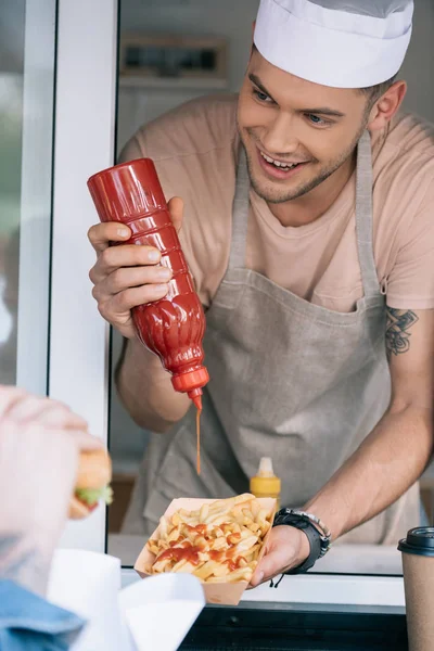 Chef sorrindo adicionando ketchup para cachorro-quente no caminhão de alimentos — Fotografia de Stock