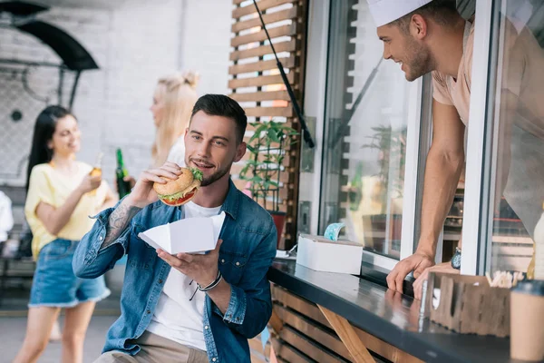 Bonito homem comer hambúrguer perto de comida caminhão — Fotografia de Stock