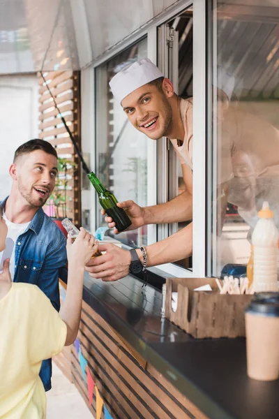 Chef sorrindo dando bebidas aos clientes do caminhão de alimentos e olhando para a câmera — Fotografia de Stock