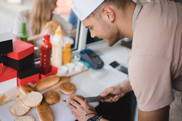 Seitenansicht Koch schneidet Brötchen mit Messer in Foodtruck — Stockfoto