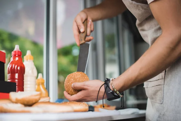 Imagen recortada de chef cortando bollo con cuchillo en camión de comida - foto de stock