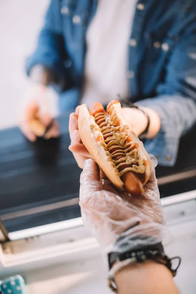 Image recadrée du chef donnant hot dog savoureux au client dans le camion alimentaire — Photo de stock