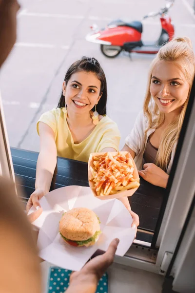 Imagem cortada de chef dando hambúrguer e batatas fritas para clientes sorridentes do caminhão de alimentos — Fotografia de Stock