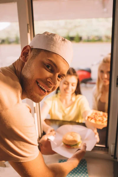 Smiling chef giving burger and french fries to customers from food truck — Stock Photo