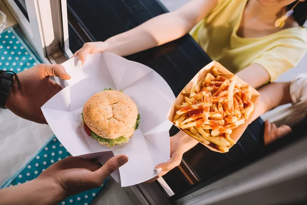 Imagen recortada de chef dando hamburguesa y papas fritas a los clientes de camión de comida - foto de stock