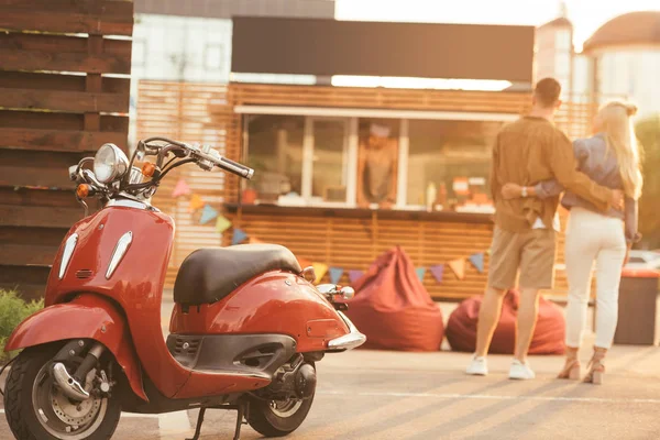 Vista trasera de la pareja de pie cerca de camión de comida con scooter en primer plano - foto de stock