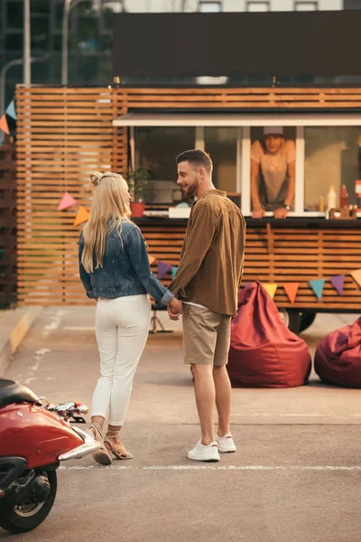 Vista trasera de pareja cogida de la mano cerca de camión de comida - foto de stock