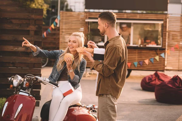 Couple eating french fries and burger near food truck, girlfriend pointing on something — Stock Photo