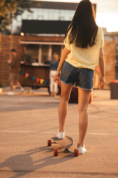 Visão traseira da menina de pé no skate perto de caminhão de comida — Fotografia de Stock