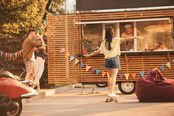 Vista posteriore della ragazza in piedi su skateboard vicino camion cibo — Foto stock