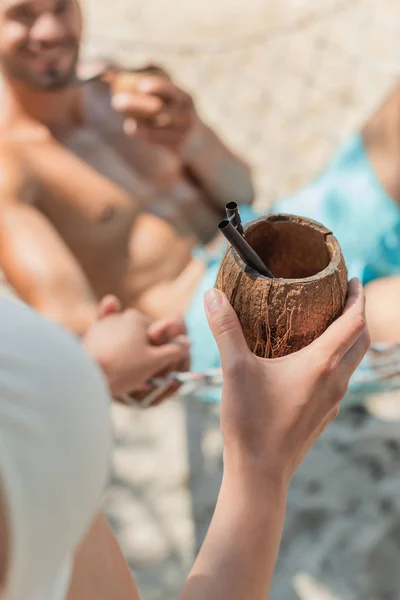 Vista recortada de la muchacha que trae coctel del coco a su novio en la hamaca, foco selectivo - foto de stock