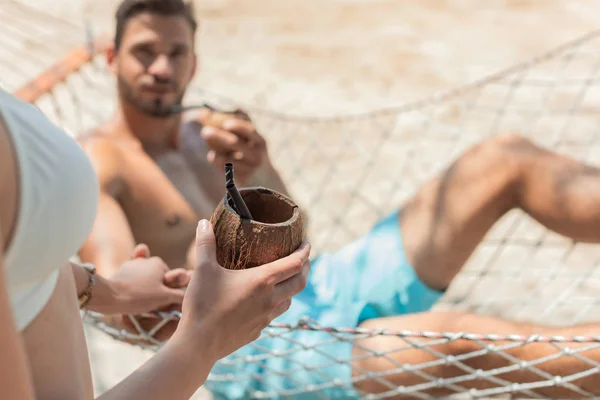 Girl with coconut cocktail holding hands with her boyfriend on hammock, selective focus — Stock Photo