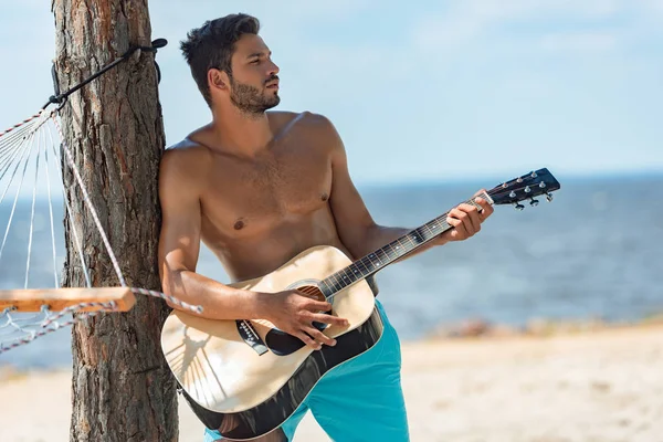 Männlicher hemdsloser Musiker spielt Akustikgitarre am Strand — Stockfoto