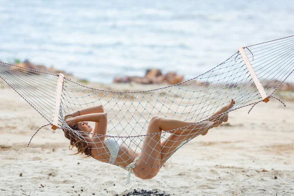 Belle jeune femme en bikini reposant sur hamac sur la plage — Photo de stock