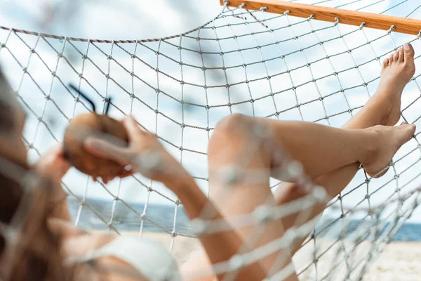 Selective focus of girl in swimsuit resting in hammock with coconut cocktail — Stock Photo