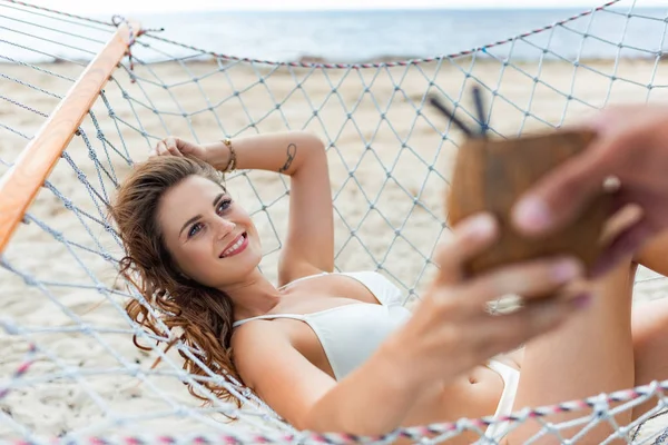 Selective focus of man giving coconut cocktail to his attractive girlfriend on hammock — Stock Photo