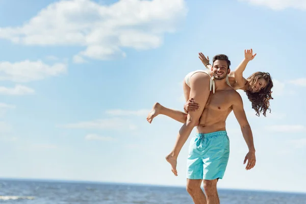 Мужчина держит подругу на плече на морском курорте, развлекаясь летом — стоковое фото
