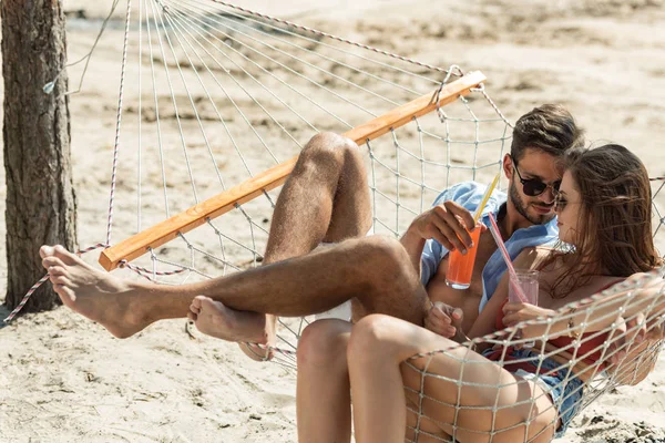 Красивая девушка и парень в солнечных очках расслабляются в гамаке с коктейлями из алкоголя — стоковое фото