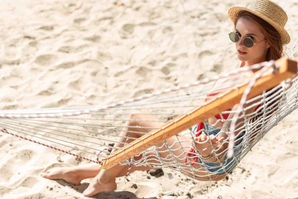 Menina atraente em chapéu de palha descansando na rede na praia arenosa — Fotografia de Stock