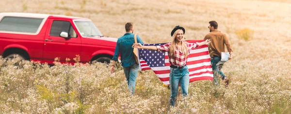 Group of young friends with united states flag in flower field during road trip — Stock Photo
