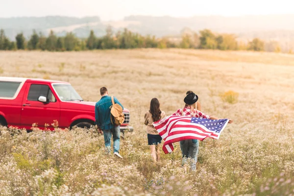 Группа молодых американцев с флагом, гуляющих по цветочному полю — стоковое фото