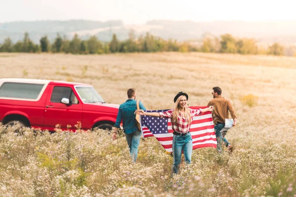 Grupo de jóvenes amigos con bandera de los estados unidos en el campo de flores durante el viaje en coche - foto de stock