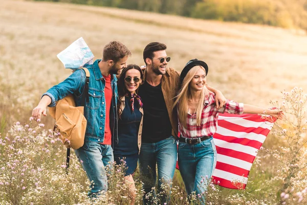 Group of smiling young american travellers with flag walking by flower field — Stock Photo