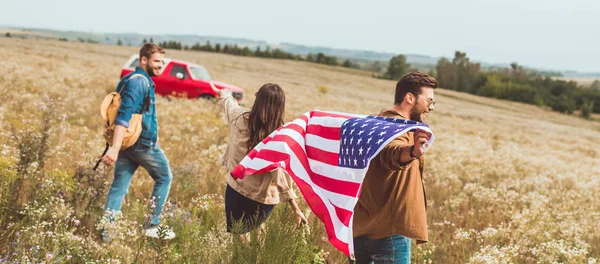 Grupo de amigos con bandera de los estados unidos en el campo de flores durante el viaje en coche — Stock Photo