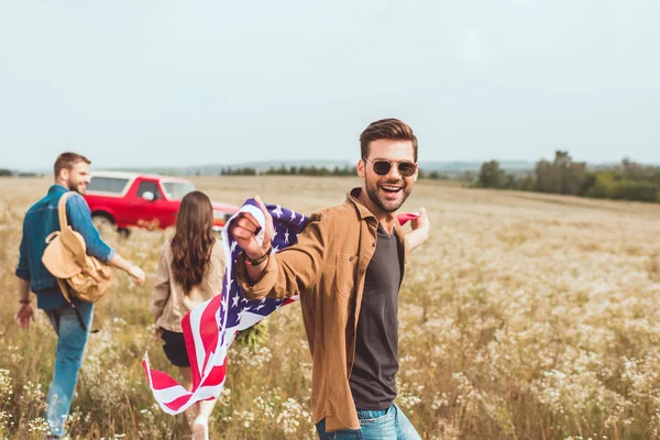 Bel giovane con gli Stati Uniti bandiera nel campo di fiori con l'amico durante il viaggio in auto — Foto stock