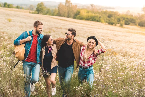 Gruppo di giovani amici felici che abbracciano e camminano sul campo insieme durante il viaggio — Foto stock