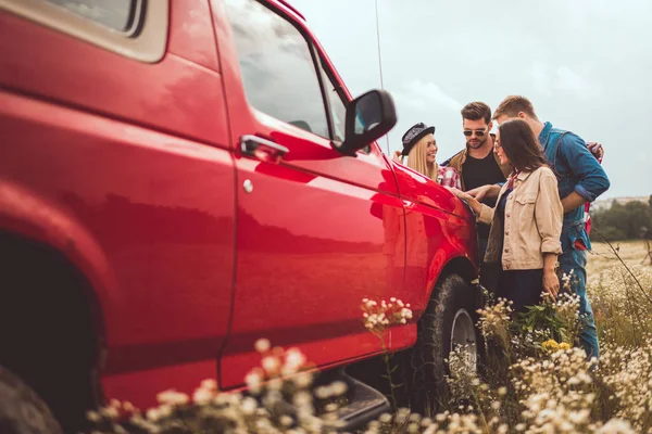 Gruppo di giovani amici che programmano viaggio in auto con mappa sul cofano motore — Foto stock